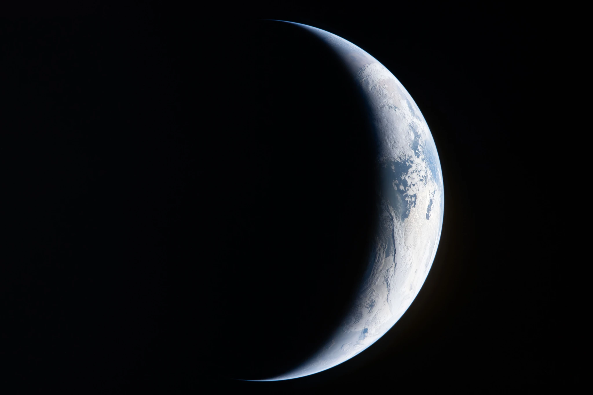 A sliver of Earth is illuminated against the blackness of space in this photo taken by an Artemis II crew member through an Orion spacecraft window.