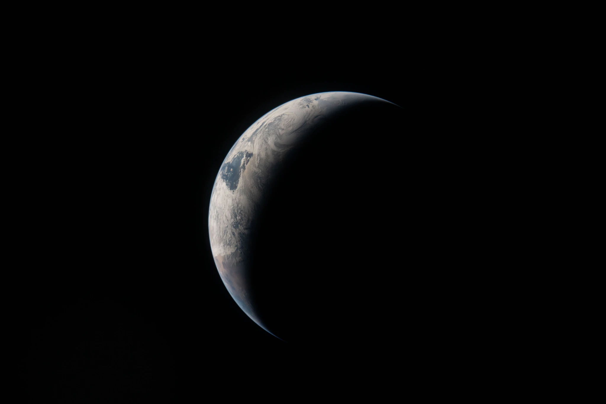 A thin arc glowing in the darkness of space. Sunlight traces the curves of the ocean and clouds, while the rest of the planet fades into shadow.