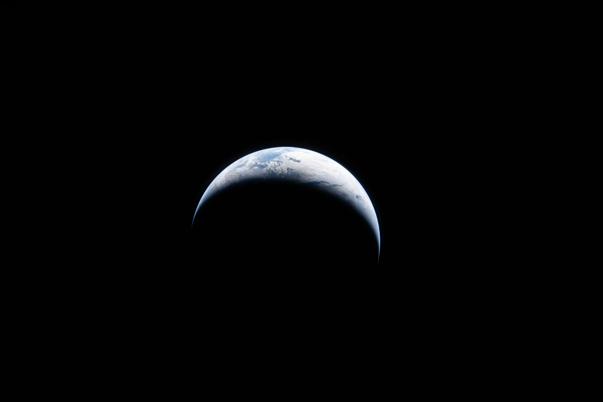 A sliver of Earth is illuminated against the blackness of space in this photo taken by an Artemis II crew member through an Orion spacecraft window.